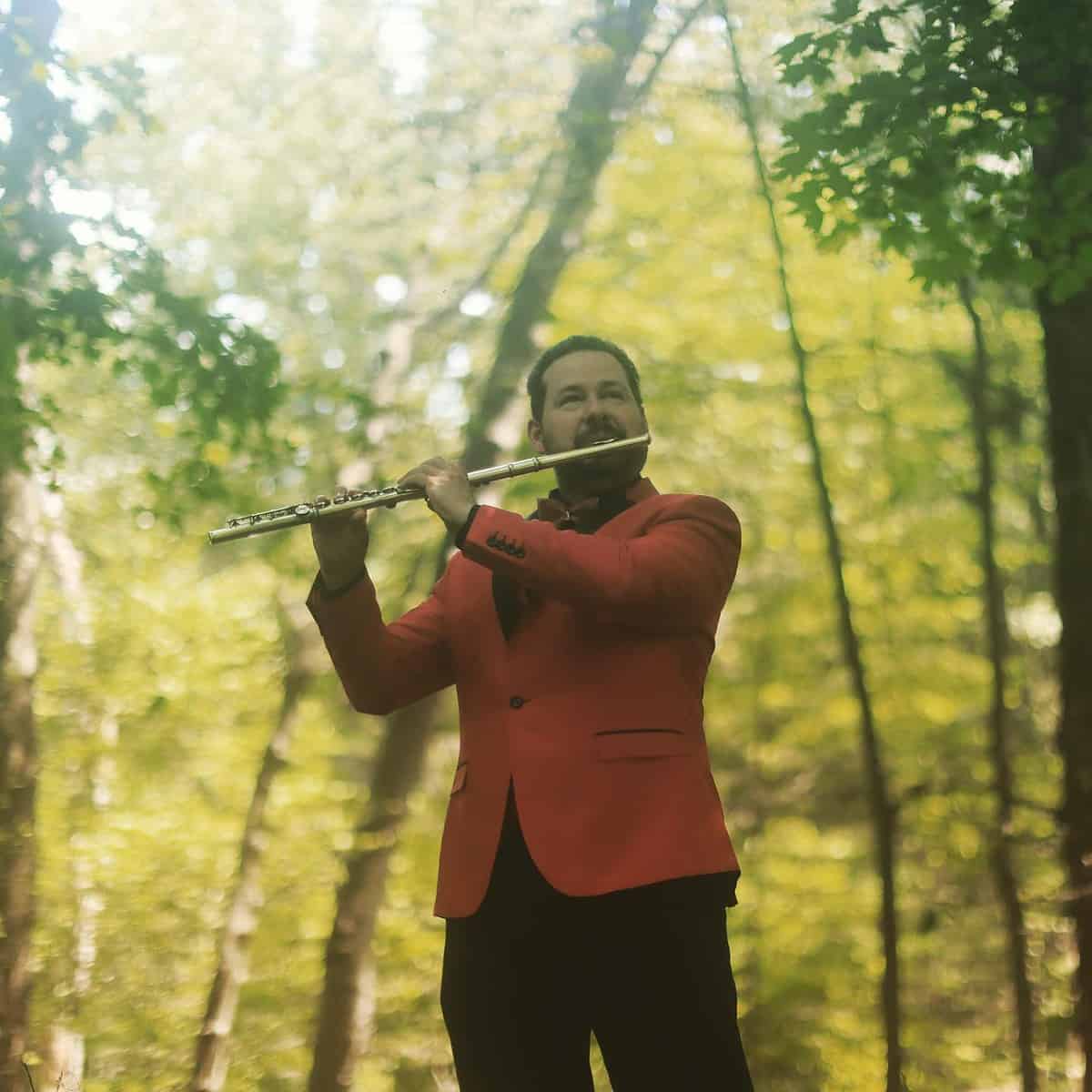 Carlos Jimenez plays the flute in a woodland setting.