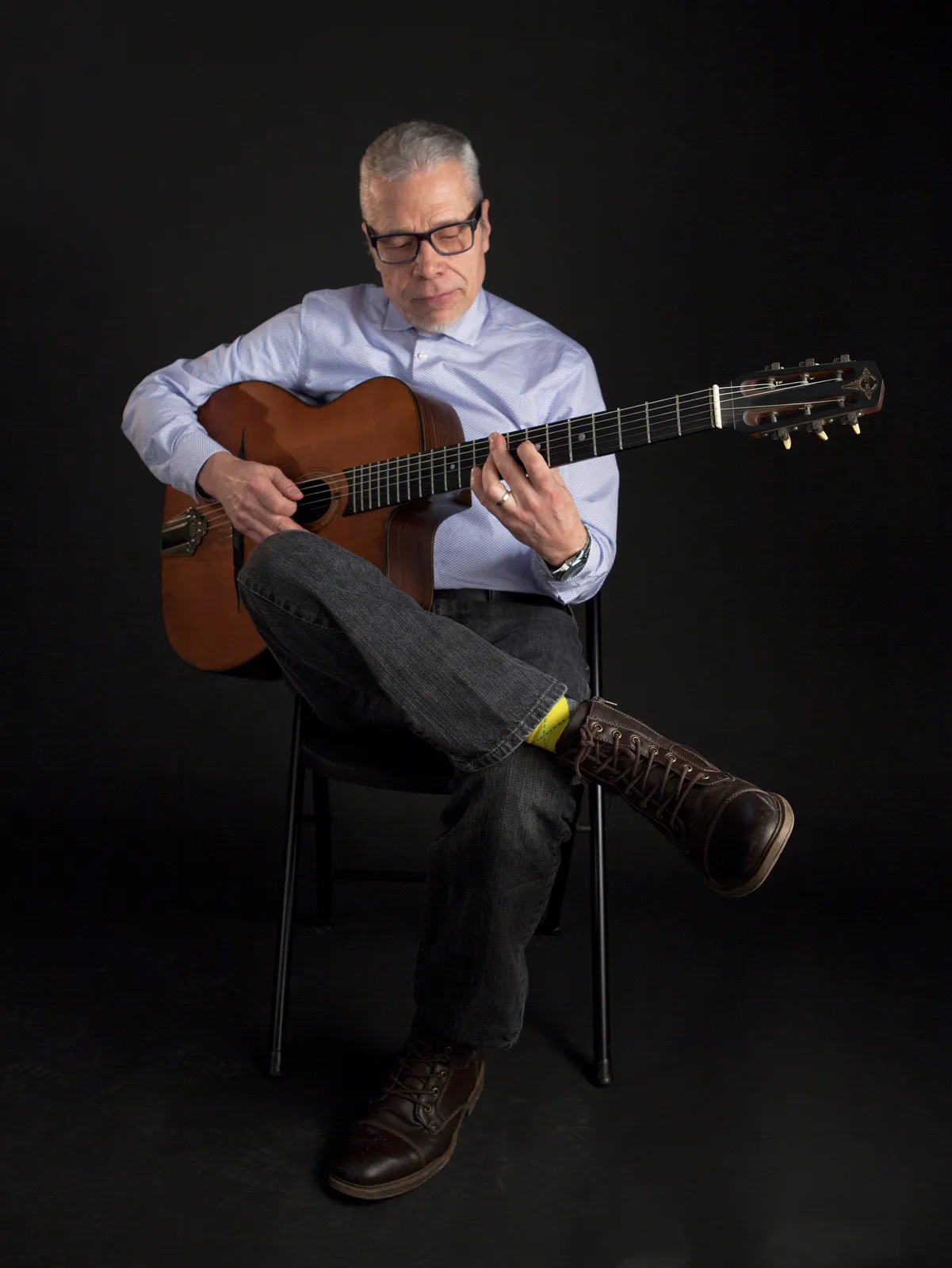 Black room portrait of Doug Munro playing a classic acoustic guitar.